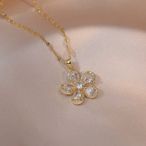 A collection of four flower pendant necklaces with gold plating, displayed on a white surface. Each pendant is crafted from titanium steel and cubic zirconia, featuring a different color combination for the gemstones.