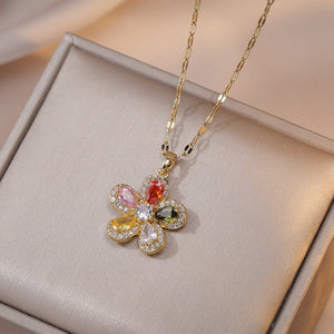 A collection of four flower pendant necklaces with gold plating, displayed on a white surface. Each pendant is crafted from titanium steel and cubic zirconia, featuring a different color combination for the gemstones.