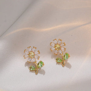 Gold flower-shaped earrings with green leaves on a light fabric background