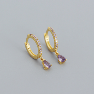 Gold hoop earrings with purple teardrop stones on a gray background