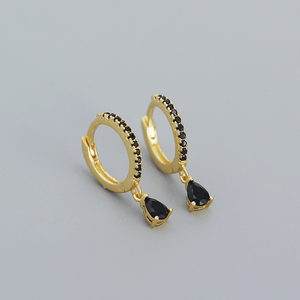 Gold hoop earrings with black teardrop charms on a gray background