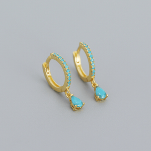Gold hoop earrings with turquoise stones on a gray background