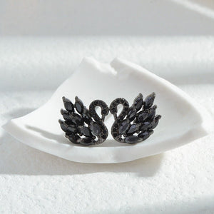 Black swan-shaped earrings on a white fabric background