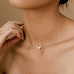 Gold necklace with a delicate pendant worn by a person against a neutral background