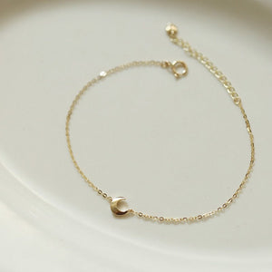 Gold bracelet with a small crescent moon charm on a light background