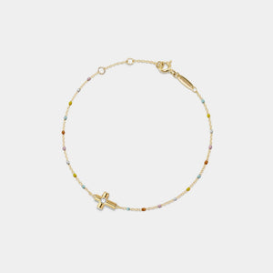 Gold bracelet with a cross charm on a light gray background