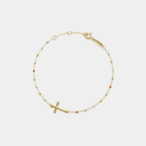 Gold bracelet with a small cross charm on a light gray background