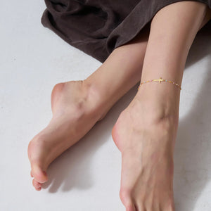 Close-up of feet wearing a gold anklet on a neutral background