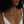 A close-up of a model wearing a delicate gold chain necklace with a small gold cross pendant featuring a dark blue stone, styled with a white camisole.