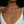 A close-up of a model wearing a delicate gold cross pendant necklace with a small dark stone at the center, styled with a white spaghetti-strap top.