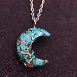 Turquoise crescent moon pendant with tree design on a dark background