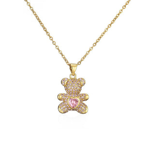 Gold teddy bear pendant with a pink heart stone on a gold chain against a white background