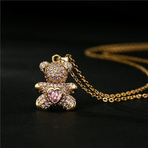 Gold teddy bear pendant with pink heart on a black background