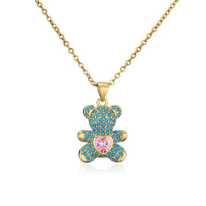 Gold teddy bear pendant with turquoise stones and a pink heart on a white background