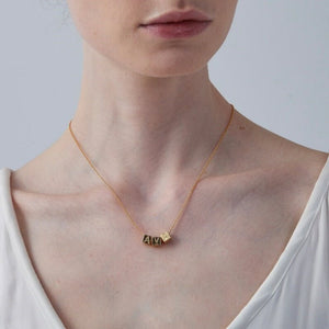 Gold necklace with a small pendant worn by a person against a neutral background
