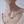 Gold necklace with a cube pendant on a person wearing a white top against a light background