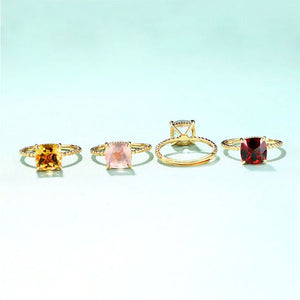 Four gold rings with different colored gemstones on a light blue background
