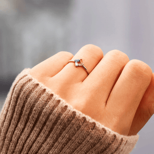 Ring with a colorful gemstone on a person's finger wearing a brown sleeve.