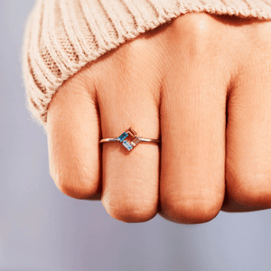 Close-up of a hand wearing a ring with colorful stones on a neutral background