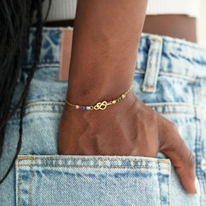 Gold anklet with colorful beads on a person's ankle wearing blue jeans.