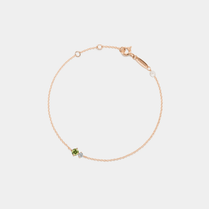 A gold-plated sterling silver bracelet featuring a small pearl charm and a red birthstone charm, connected by a fine chain.