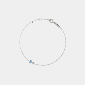 A gold-plated sterling silver bracelet featuring a small pearl charm and a red birthstone charm, connected by a fine chain.
