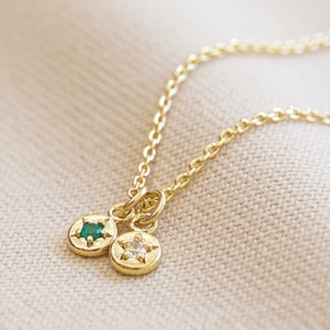 Gold necklace with two round pendants on a beige fabric background