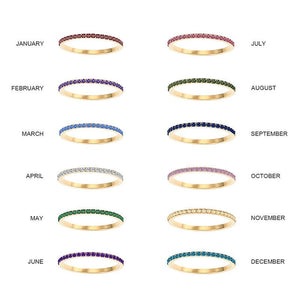 Gold rings with colored gemstones for each month of the year on a white background.