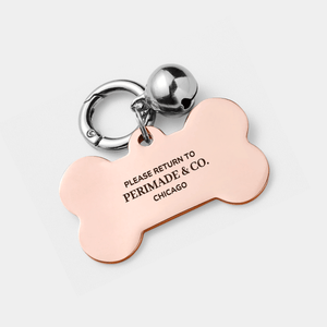 Dog tag shaped like a bone with 'Please return to Permade & Co. Chicago' text on a light gray background