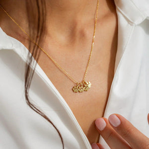 Gold necklace with a leaf-shaped pendant worn by a person in a white shirt.