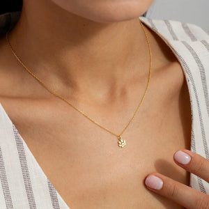 Gold necklace with a small pendant worn by a person, with a neutral background