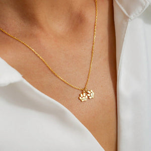 Gold necklace with a paw print pendant on a person wearing a white shirt.
