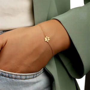 Gold bracelet with a paw print design on a wrist, wearing a green jacket and light blue jeans.