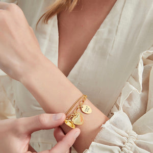 Woman wearing a gold bracelet with heart locket and 'Love P & Co' tag on a white background