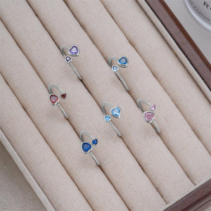 Set of silver rings with heart-shaped gemstones on a beige fabric surface