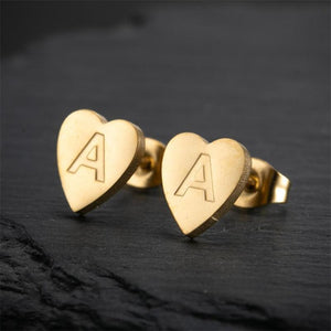 Gold heart-shaped earrings with 'A' engraving on a dark background