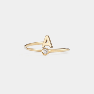 Gold ring with letter 'A' and small diamond on a light gray background