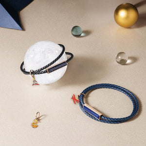 Blue braided bracelet with a small charm on a beige surface with decorative objects.