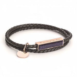 Black braided leather bracelet with rose gold tag and heart charm on a white background