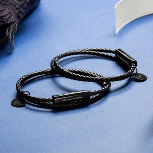 Black braided bracelet with metal tags on a blue surface