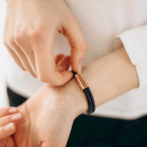 Person adjusting a black bracelet with a rose gold clasp on a white background