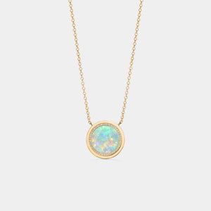 Gold plated round locket necklace featuring a opal center with a halo of small clear stones, on a delicate chain against a white background.