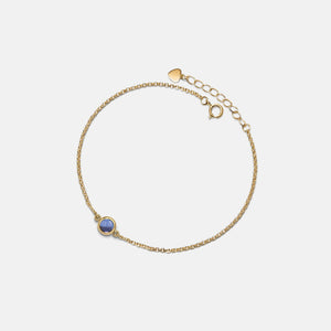 Gold bracelet with a blue gemstone on a light gray background