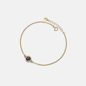 Gold bracelet with a dark gemstone on a light gray background