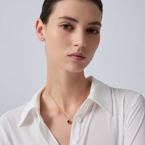 Woman wearing a white shirt and gold necklace with a dark pendant on a light gray background