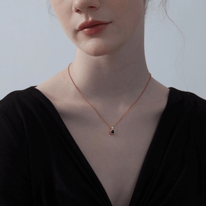 Woman wearing a gold necklace with a projection gemstone pendant on a light gray background