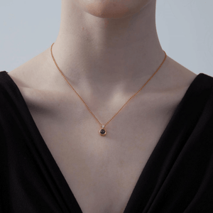 Woman wearing a gold necklace with a projection gemstone pendant on a light gray background