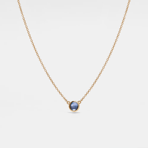 Gold necklace with a blue gemstone on a light gray background