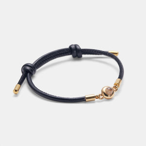 Navy blue leather bracelet with gold accents on a light gray background