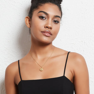 A model wearing a gold necklace with a round locket pendant on a light gray background